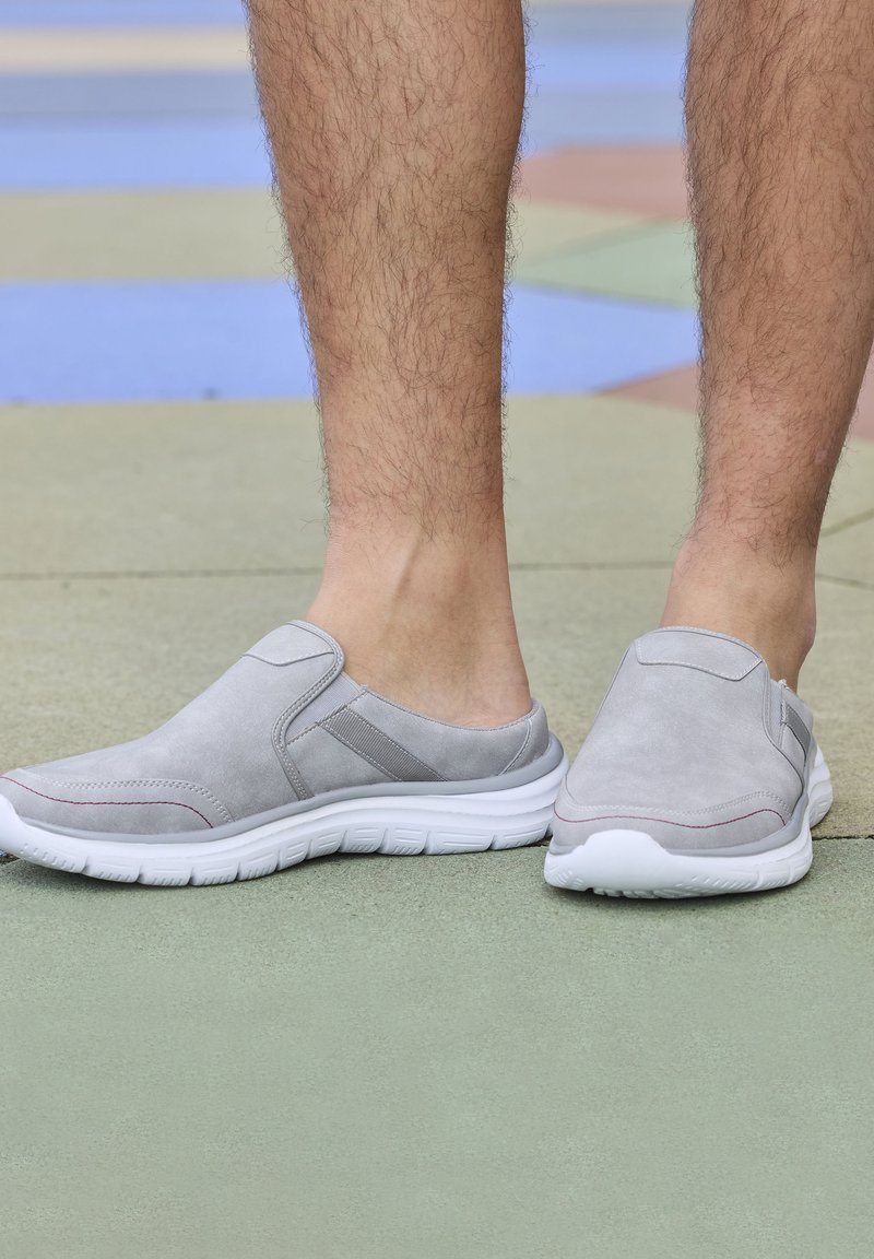 Gray slip-on shoes with suede texture, white rubber soles, and subtle red accents. The design features elastic side panels for easy wear.