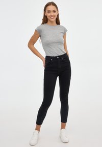 Camiseta gris ajustada combinada con jeans skinny negros de tiro alto. La modelo lleva zapatillas blancas. Diseño simple y sin costuras, textura suave.
