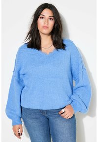 Pull en maille bleu clair avec un décolleté en V, des épaules tombantes et un tissu texturé ; associé à un jean ajusté. Manches longues et volumineuses.