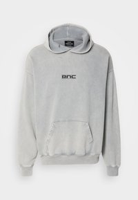 Sudadera gris claro con capucha, bolsillo frontal, puños y dobladillo acanalados; presenta un logo impreso en negro "mnc" en el pecho. Material de algodón.