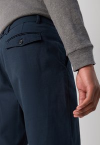 Tamnoplave pamučne hlače imaju stražnji džep na gumbe, elegantan dizajn, glatku teksturu i bočni džep vidljiv uz nogu.