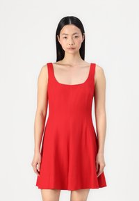 Robe rouge sans manches présentant un décolleté carr�é, un corsage ajusté et une jupe évasée. Fabriquée en tissu léger avec une texture lisse.