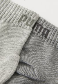 Sive čarape s rebrastim manžetama, izrađene od mekanog materijala, s "Puma" logom u kontrastnim bojama na vrhu.
