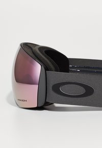 Occhiali da sci neri con lente rosa, imbottitura in foam flessibile e un cinturino grigio scuro con un logo ovale. Lente etichettata "Prizm."