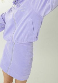 Ljuslila velour zip-up jacka med texten "Keep it Real", elastisk midja och matchande minikjol med framdragkedja och ficka.