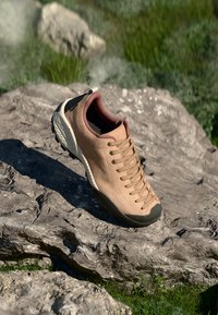 Hellbrauner Wildlederschuh mit einer dunkelgrauen Gummisohle, runder Zehenform und braunen Schnürsenkeln. Er verfügt über eine strukturierte Oberfläche und einen gepolsterten Schaftrand.