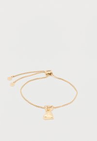 Pulsera de cadena dorada con un charm en forma de corazón. Cierre ajustable con un acabado liso y brillante. Incluye dos discos decorativos cerca del broche.