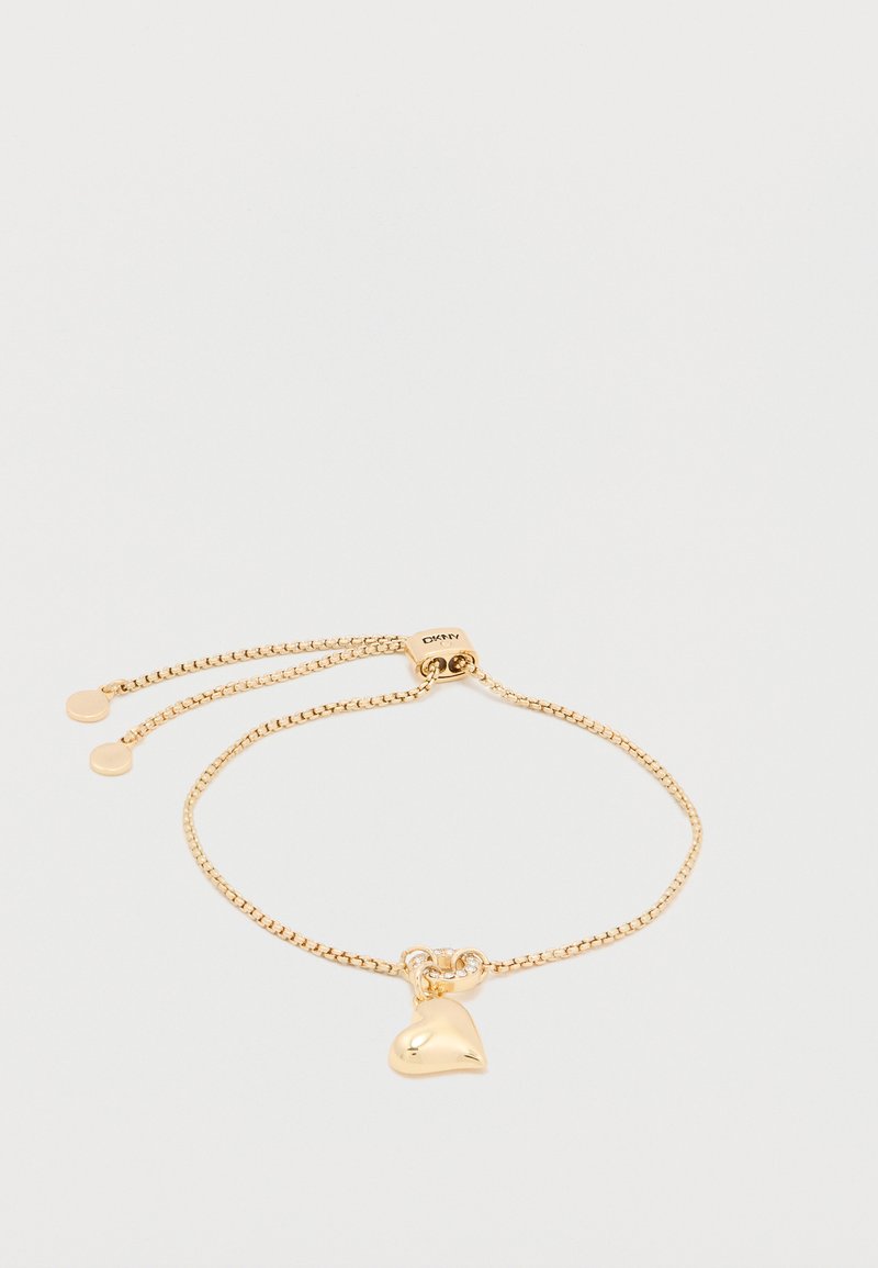 Pulsera de cadena dorada con un charm en forma de corazón. Cierre ajustable con un acabado liso y brillante. Incluye dos discos decorativos cerca del broche.