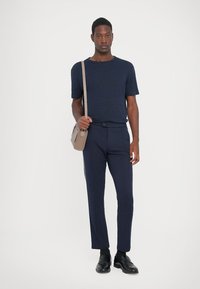 Marineblaue kurzärmlige T-Shirt und schmal geschnittene marineblaue Hose; glattes Material; kombiniert mit einer hellbraunen Umhängetasche und schwarzen Schuhen.