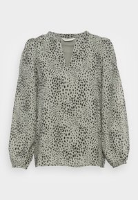 Ljust grön blus med V-hals, långa puffärmar och ett svart prickmönster över hela tyget. Mjuk, slät textur.