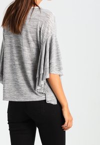 Grijs, T-shirt met korte mouwen en uitlopende ruffle-details op de mouwen, gemaakt van zacht, gestructureerd materiaal. Draag het met zwarte broeken voor een casual uitstraling.