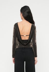 Μπλούζα με μακριά μανίκια από σκούρο μεταλλικό ύφασμα με σχεδιασμό πλάτης με δίπλωμα και στενό κλείσιμο στη μέση, συνδυασμένη με μαύρο τζιν φαρδύ πόδι.