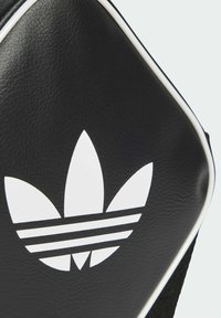 Musta teksturoidut laukku, jossa on suuri valkoinen Adidas Trefoil -logo ja valkoiset reunapaneelit.