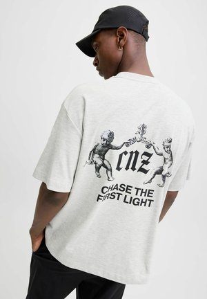 Camiseta de algodón gris claro con un corte relajado. Presenta una impresión gráfica de querubines y el texto "cmz CHASE THE FIRST LIGHT" en la parte posterior.