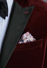 Bordo baršunasti blejzer s crnim satenastim reverima, s svilenim džepnim rupcem s cvjetnim uzorkom u nijansama crvene i krem. 