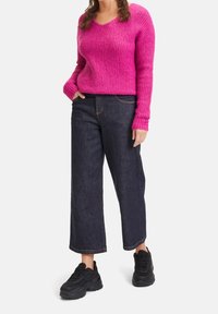 Fuchsiastricken tröja med V-ringning, tillsammans med mörka vida denimbyxor och svarta klumpiga sneakers. Strukturerad tyg med ribbat mönster.