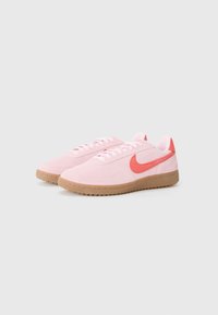 Rosa semskesko med gummisåle, med en korallfarget Nike-skjerm, rosa snørebånd og glatt tekstur på overflaten.