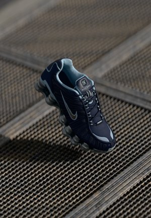 Tumedas sinises Nike Shox jalatsid hõbedaste aktsentidega ja pehme tallaga tekstuurilisel metallvõrgupinnal.