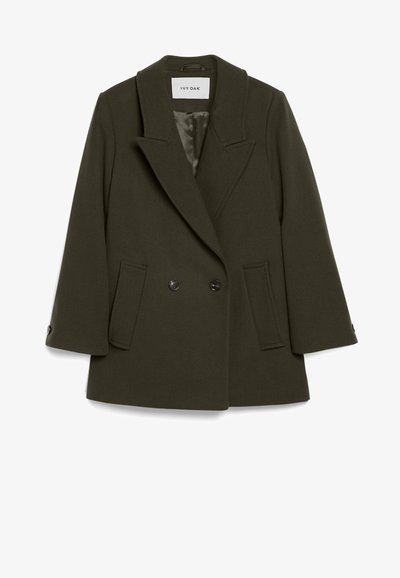 Σκούρο πράσινο, διπλής όψης παλτό από μάλλινο ύφασμα με γωνιώδη γιακά, δύο μπροστινές τσέπες και κουμπιά στα μανίκια. Λείο εσωτερικό φόδρας.