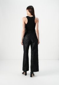 Black tank top paired with high-waisted, black floral-textured pants. The fabric features raised patterns and a flowing wide-leg silhouette.