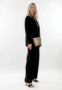 Traje negro a medida con pantalones de pierna ancha, llevado sobre una blusa blanca. También se presentan un bolso cruzado metálico dorado y sandalias de tacón negro.