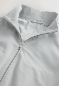 Light grey zip-up jacket with a raised collar, partially unzipped to show smooth inner lining and a size M label.