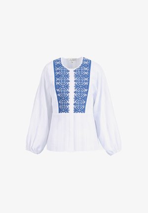 Blouse blanche à manches longues avec broderie florale géométrique bleue sur le panneau avant et poignets élastiques froncés.