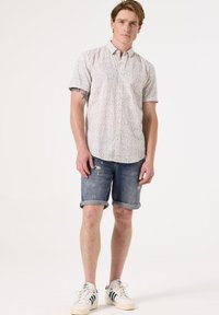 Korte mouw knoopshirt met een bloemenpatroon, gecombineerd met versleten denim shorts en witte sneakers met groene accenten.