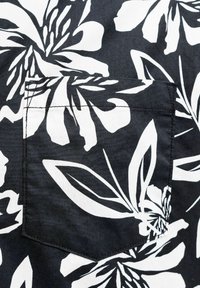 Musta kangas, jossa on suuri valkoinen trooppinen kukkakuosi, ja pinnalla ommeltu vastaava painettu pikkutasku.