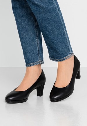 Czarne skórzane buty na wysokim obcasie z okrągłym noskiem i gładką teksturą, połączone z krótkimi niebieskimi dżinsami.