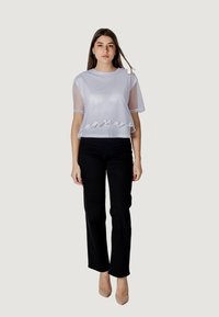 Camiseta blanca corta con mangas semitransparentes, con un dobladillo ondulado. Combinada con pantalones rectos negros y tacones nude.