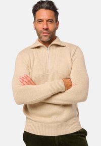 Beige Strickpullover mit Reißverschluss, gerippten Bündchen und Saum. Verfügt über ein strukturiertes Muster auf der Brust, hergestellt aus weichem Stoff.