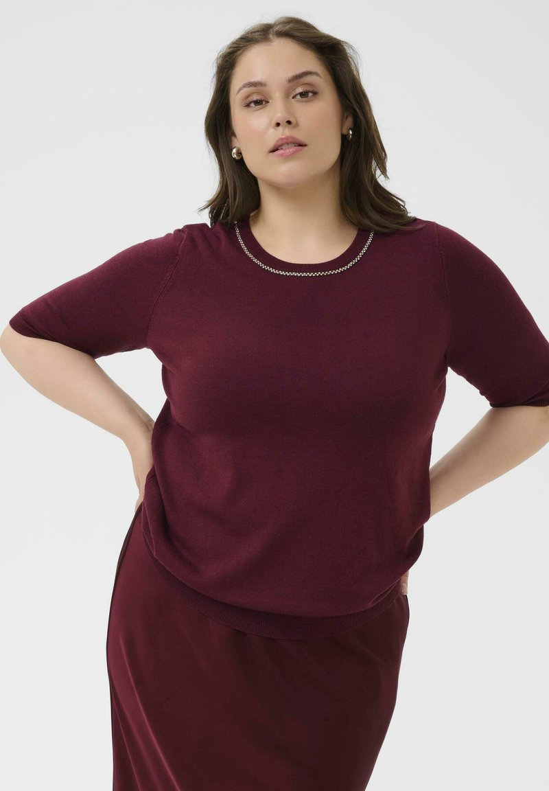 Pull bourgogne à manches courtes avec un col rond accentué par un détail en chaîne. Tissu lisse, coupe décontractée, associé à une jupe assortie.