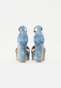 Denim plattform hæler med åpen bak, i en lys blå farge, med pregete mønster og spenne lukking på ankelremmen.