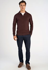 Bordowy sweter z długim rękawem i dekoltem w serek, z ribbed mankietami, w połączeniu z granatowymi spodniami i brązowymi butami typu boat shoes. Gładka faktura, dopasowany krój.