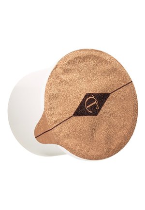 Conteneur blanc avec un couvercle en cuivre texturé. Le couvercle présente une forme de diamant sombre et un logo stylisé au centre. Surface lisse.