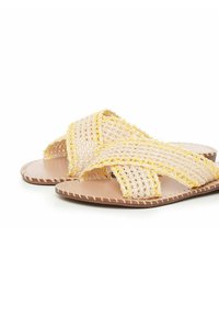 Sandalias de color beige trenzadas con correas cruzadas y acentos en amarillo, suela plana y acabado texturizado. Ideales para uso casual.