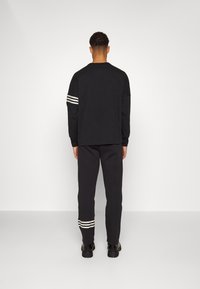 Černé tričko s dlouhým rukávem a černé kalhoty s bílými pruhy. Měkká, ležérní látka. Jednoduchý, volný střih s minimalistickým designem.