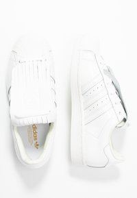 Vita lädersneakers med rund tå, tre grå ränder, unik flik tunga och vita snören. Har en texturerad gummisula.