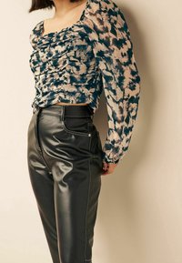 Gerimpelde bloes in een blauw en beige patroon; doorzichtige lange mouwen. Zwarte neplederen hoge taille broek met witte stiksels en zakken.