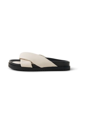 Sandale beige et noire à enfiler avec larges brides croisées rembourrées et semelle plate rainurée sur fond blanc.