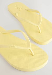 Gele flip-flops met een gestructureerd oppervlak, voorzien van dunne banden en een gevormd voetbed. De merknaam is in de band geperst.