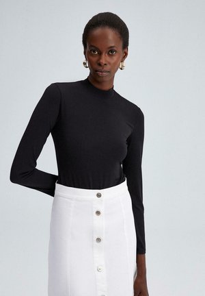 Top negru cu mâneci lungi și guler înalt, purtat cu o fustă albă cu nasturi, dotată cu accesorii din argint și un croi drept.