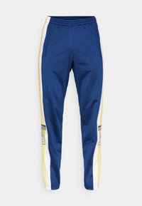 Marinblå joggerbyxor med gula och vita sidsömmer, elastisk midja, fickor med dragkedja och Adidas-logotypdetalj på vänster lår.