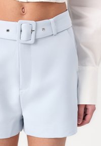 Pantaloni corti azzurri realizzati in tessuto morbido, dotati di una cintura larga con fibbia quadrata, tasche laterali e una vestibilità su misura.