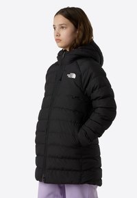Manteau rembourré noir avec capuche, fermeture zippée et poches latérales. Branding discret sur la poitrine, texture matelassée et design mi-long.