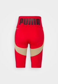Sarkani sporta šorti ar augstu jostas vietu, kurā ir liels melns "PUMA" emblēma. Zelta akcenti ap augšstilba zonu. Gluda, stiepjas auduma.