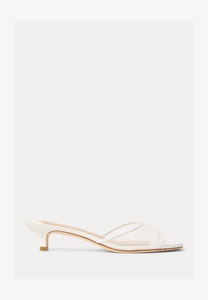 Mule blanche à talon bas avec empeigne en mesh transparent et fine lanière au niveau des orteils, semelle intérieure beige et talon fin empilé.