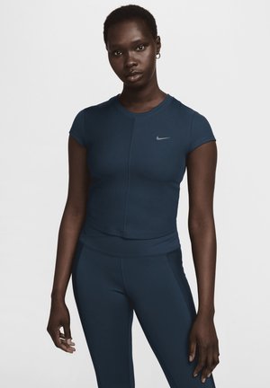 Tamno plava sportska majica s kratkim rukavima, teksturirana tkanina i suptilni srebrni Nike logo. Uparena s odgovarajućim tamnoplavim tajicama, glatke teksture.