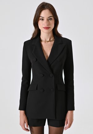 Zwart dubbelzijdig colbert met spitse revers, twee voorzakken en ronde knopen, gecombineerd met een zwart short pak. Glad textuur.